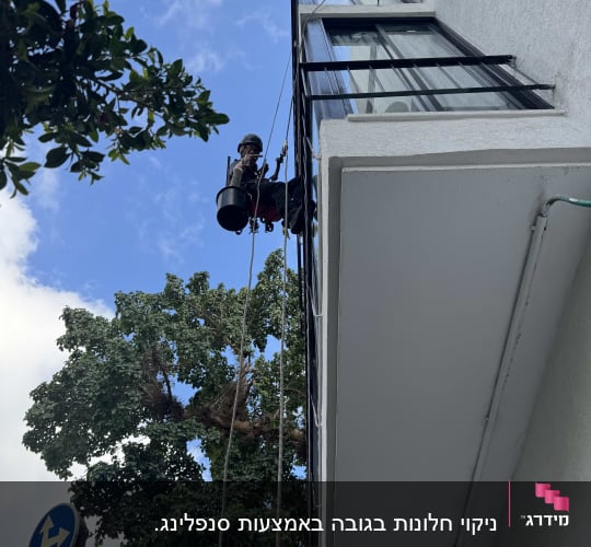 אדם עובד בגובה על בניין עם חבלים וציוד בטיחות